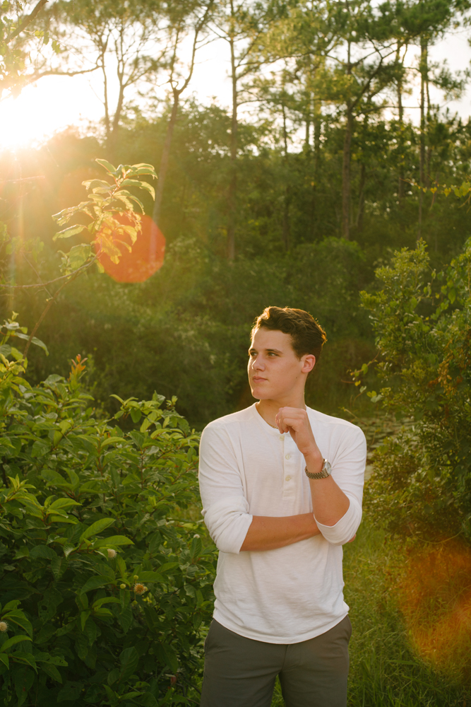 teenage boy in white shirt looking off into the distance standing in the forest